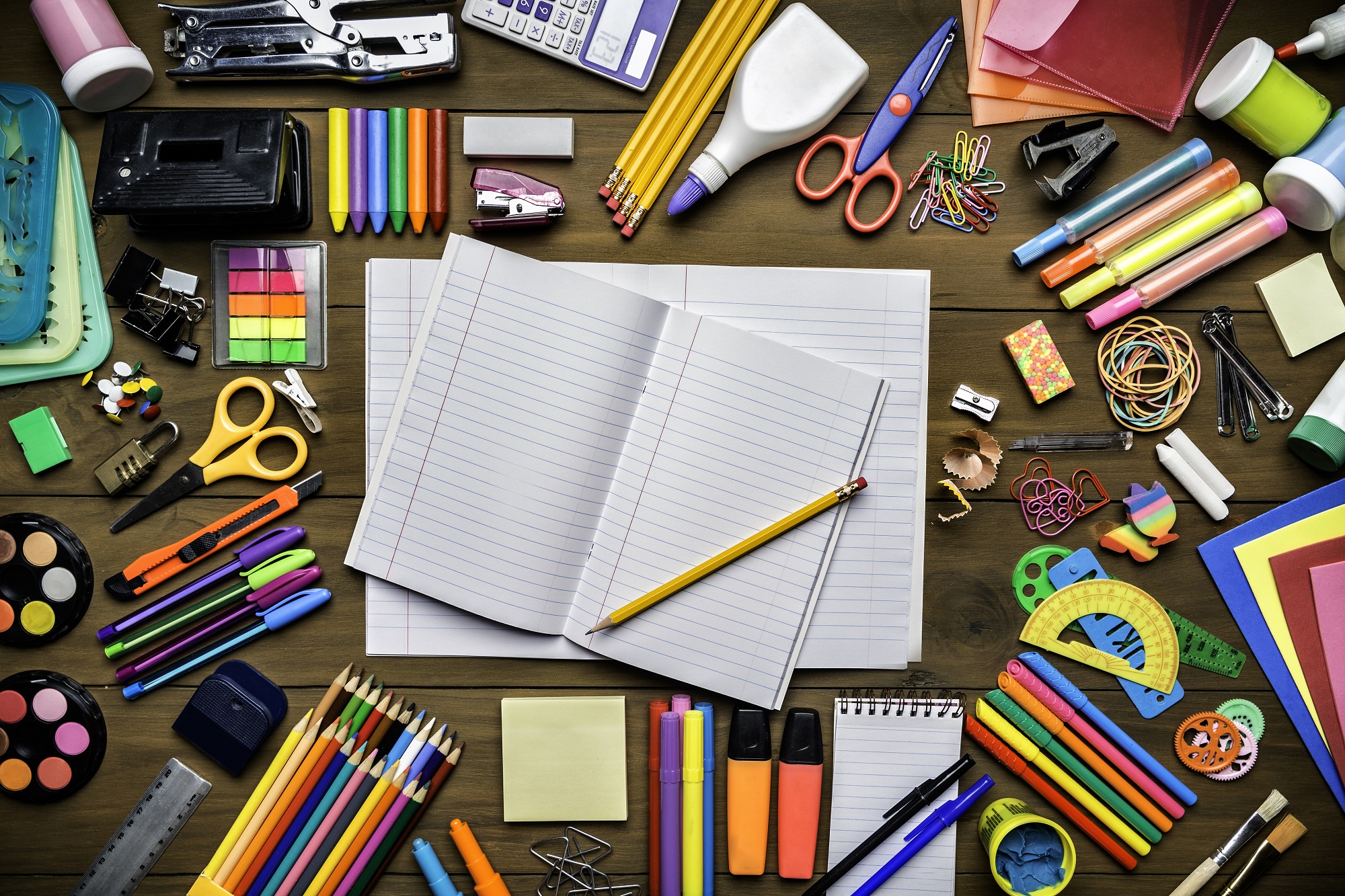 Overhead shot of stationery on wood desk with paper notepad and frame of school office supplies